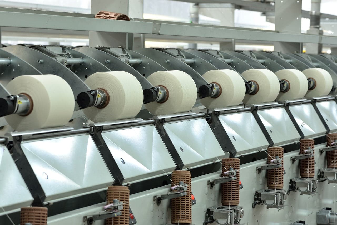 Circular knitting machine feeding cones of white yarn into fabric